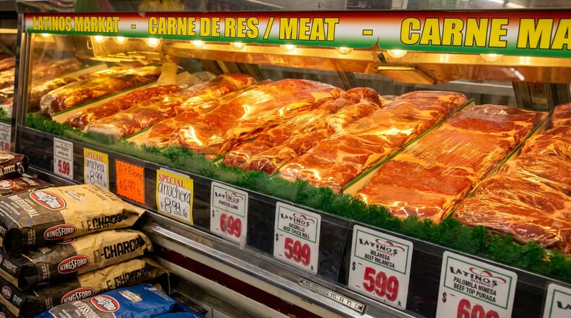 Latinos Markat meat counter showcasing various packaged raw beef cuts with price tags and charcoal.