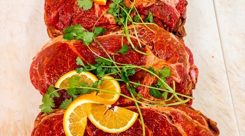 Marinated raw meat cuts topped with fresh orange slices and cilantro on a white surface.