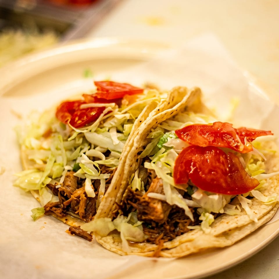 Two tacos filled with meat, shredded lettuce, and diced tomatoes on a plate.