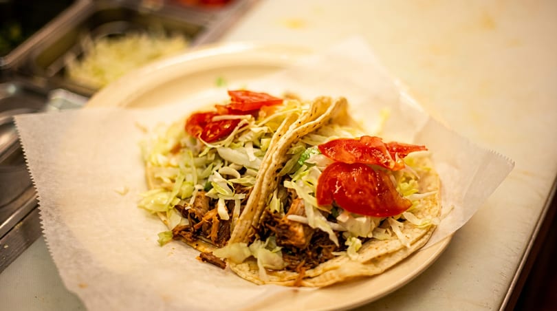 Two tacos filled with meat, shredded lettuce, and diced tomatoes on a plate.
