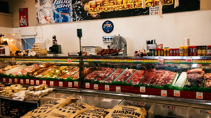 A butcher shop's refrigerated display cases showcase various fresh raw meats, spices, and charcoal for BBQ.